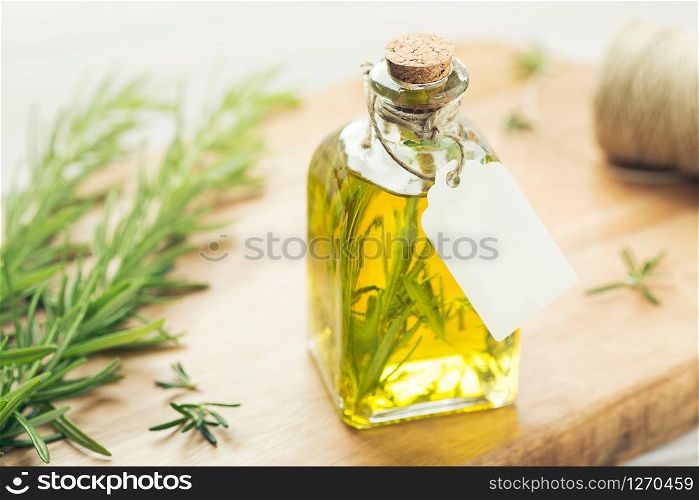 Rosemary essential oil with tag, fresh twig on wooden background. Mock up