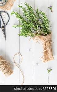 Rosemary sprigs bunch nestled inside a burlap bag tied with twine on wooden background. Fresh organic herbs with copy space for text
