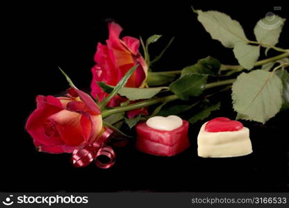 Roses on black background with two valentine heart chocolates