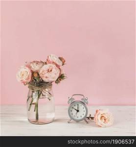 roses vase near alarm clock wooden desk against pink background. High resolution photo. roses vase near alarm clock wooden desk against pink background. High quality photo