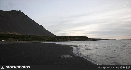 Rosy cloud atmosphere, volcanic mountain next to seashore and gentle waves