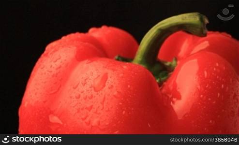 Rotation of red pepper. Under drops and on black background.