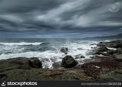Rough seas crashing into rocks near Bosa on the west coast of Sardinia with dark clouds and moody skies overhead