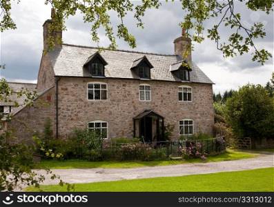 Rough stone house with dormer windows and surrounding flowers and roses
