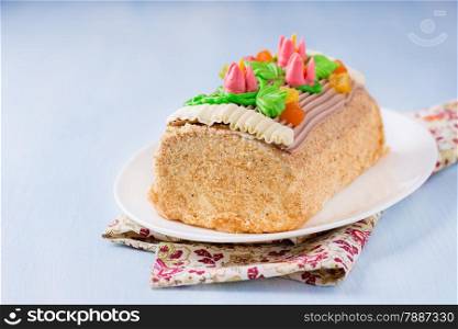 Roulade cake, decorated with colourful buttercream flowers. Yule Log Cake over light blue background. Selective focus