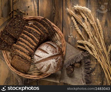 Round and sliced bread in a wicker tray with spikelets wooden surface with cloth. loaf of bread top view
