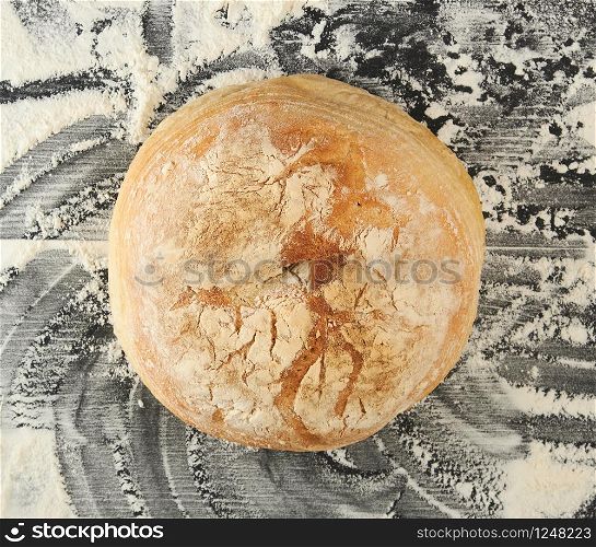 round baked bread and white wheat flour scattered on a black table, top view
