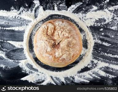 round baked bread and white wheat flour scattered on a black table, top view