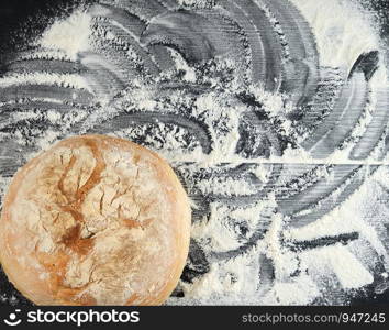 round baked bread and white wheat flour scattered on a black table, top view