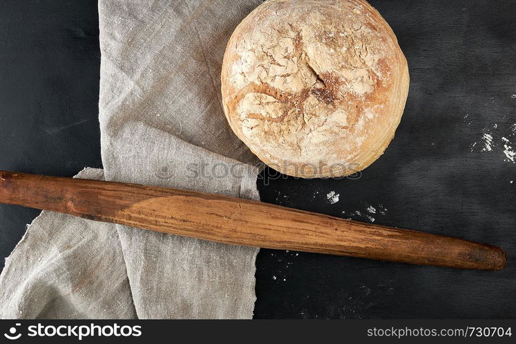 round baked bread and wooden old rolling pin on a black table, top view