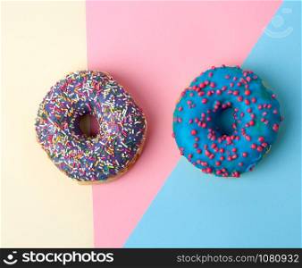round baked donut with colored sugar sprinkles and with blue sugar glaze on a pink-yellow background, top view