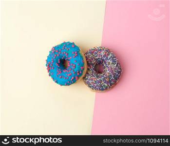 round baked donut with colored sugar sprinkles and with blue sugar glaze on a pink-yellow background, top view