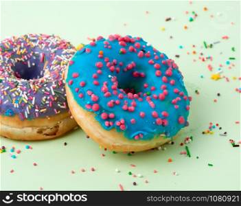 round baked donut with colored sugar sprinkles and with blue sugar icing on a green background, close up