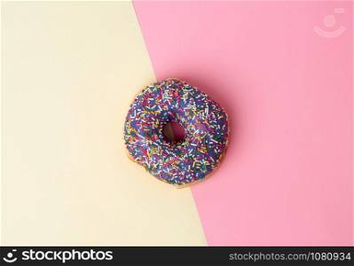 round baked donut with colored sugar sprinkles on a pink-yellow background, top view