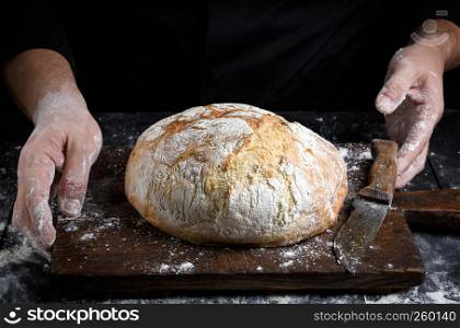 round baked homemade bread on an old brown wooden board and chef hands
