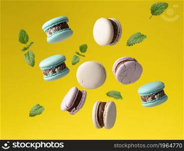 round baked macarons levitate on a yellow background, green mint leaves are flying around