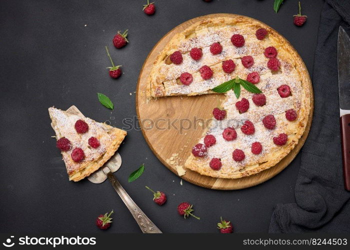 Round baked pie with apples and sprinkled with powdered sugar on a black table. View from above