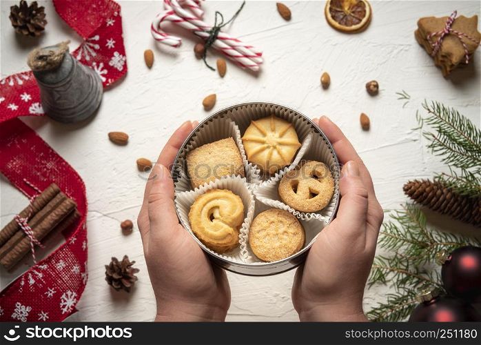 Round box filled with cookies in a woman's hands. Above view of a table full of Christmas goodies and decorations