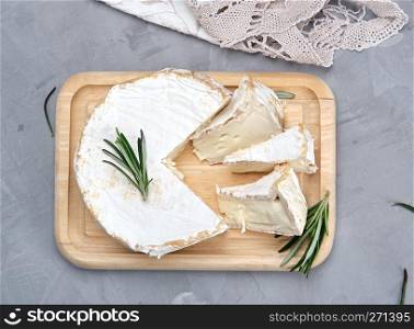 round brie cheese on a wooden board and a gray background , top view
