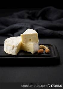 round brie cheese on brown wooden cutting board, black background