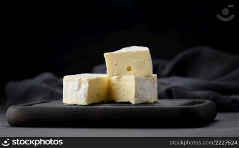 round brie cheese on brown wooden cutting board, black background