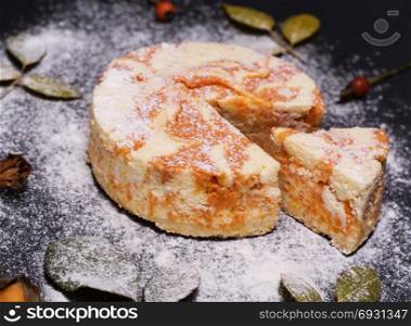 round cheesecake with pumpkin sprinkled with powdered sugar on a black background, top view