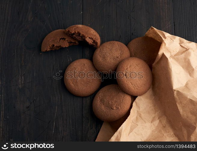 round chocolate chip cookies lie on a brown wooden table, dessert spilled out of a paper bag, top view