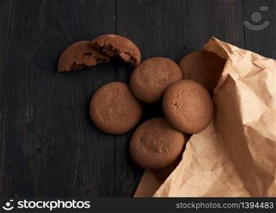 round chocolate chip cookies lie on a brown wooden table, dessert spilled out of a paper bag, top view