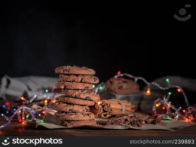 round chocolate cookies in a stack, around the New Year&rsquo;s burning garlands on a brown table