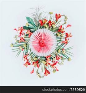 Round circle composing of tropical leaves and exotic flowers with paper party fan on white background, top view. Copy space. Floral layout