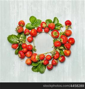 Round circle frame of strawberries with green leaves and flowers on wooden background, top view, place for text