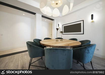 Round dining table in raw wood varnish surrounded by blue velvet upholstered armchairs under a designer l&