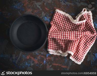 round empty black cast-iron frying pan with a red napkin in a red box on a brown worn background, top view