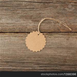 Round empty brown paper tag tied with white string. Price tag, gift tag, sale tag on the gray wooden background, close up