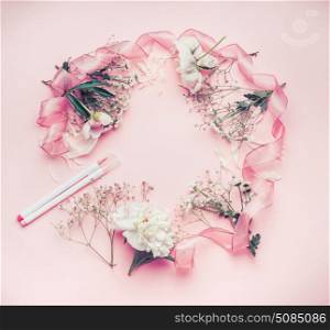 Round floral frame arrangement with pastel pink flowers, markers and ribbon, top view.
