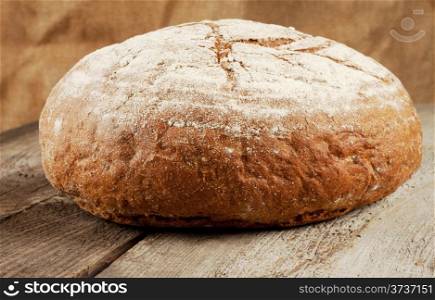 Round loaf of black bread on a wooden background