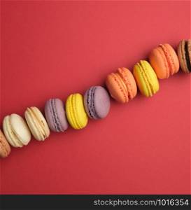 round multi-colored baked macarons with cream lie in a line on a red background, flat lay, copy space