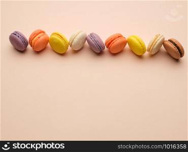round multi-colored baked macarons with cream lie in a line on a beige background, flat lay, copy space