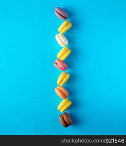 round multi-colored baked macarons with cream lie in a line on a blue background, flat lay