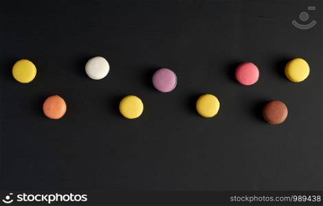 round multi-colored baked macarons with cream lie in a line on a black background, flat lay