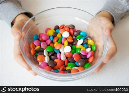 Round, multi-colored candies. Candy close-up, in a glass container. The child is holding candy.. Round, multi-colored candies. Candy close-up, in a glass container.