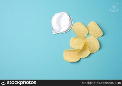 round potato chips and foil lid on blue background, top view. Copy space