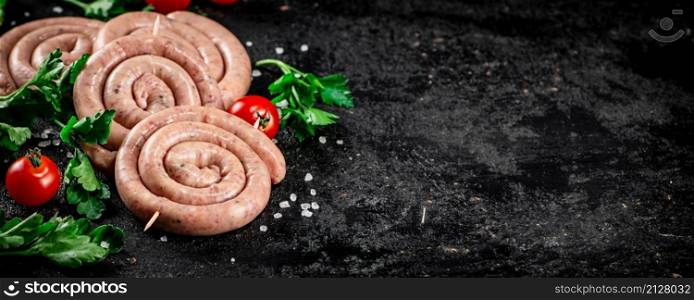 Round raw sausages with tomatoes and parsley. On a black background. High quality photo. Round raw sausages with tomatoes and parsley.