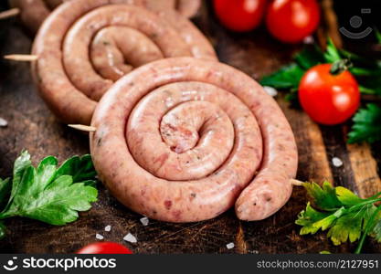 Round raw sausages with tomatoes and parsley. On a rustic background. High quality photo. Round raw sausages with tomatoes and parsley.