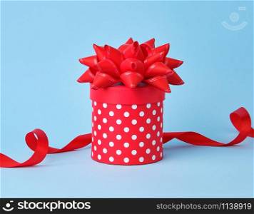 round red cardboard box in white polka dots on top of a bow on a blue background, holiday backdrop