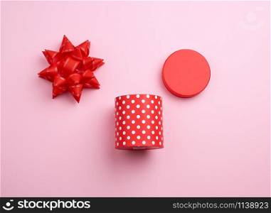 round red cardboard box in white polka dots on top of a bow on a pink background, holiday backdrop