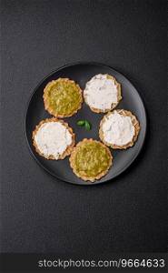 Round snacks with crispy chips or crackers with cream cheese and pesto on a ceramic plate