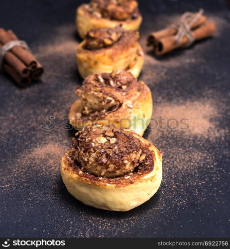 round sweet buns with cinnamon and walnut on a black background, selective focus