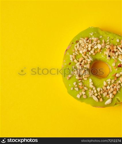 round sweet green pistachio donut sprinkled with ground nut on a yellow background, top view