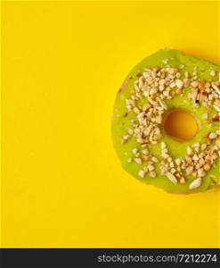 round sweet green pistachio donut sprinkled with ground nut on a yellow background, top view